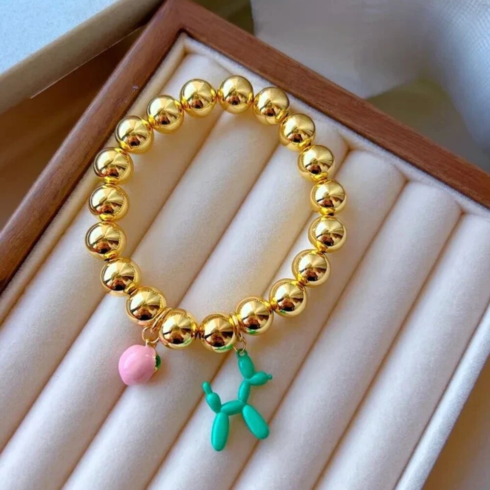 Copper bracelets plated in 18-karat gold with enameled peach and dog charms